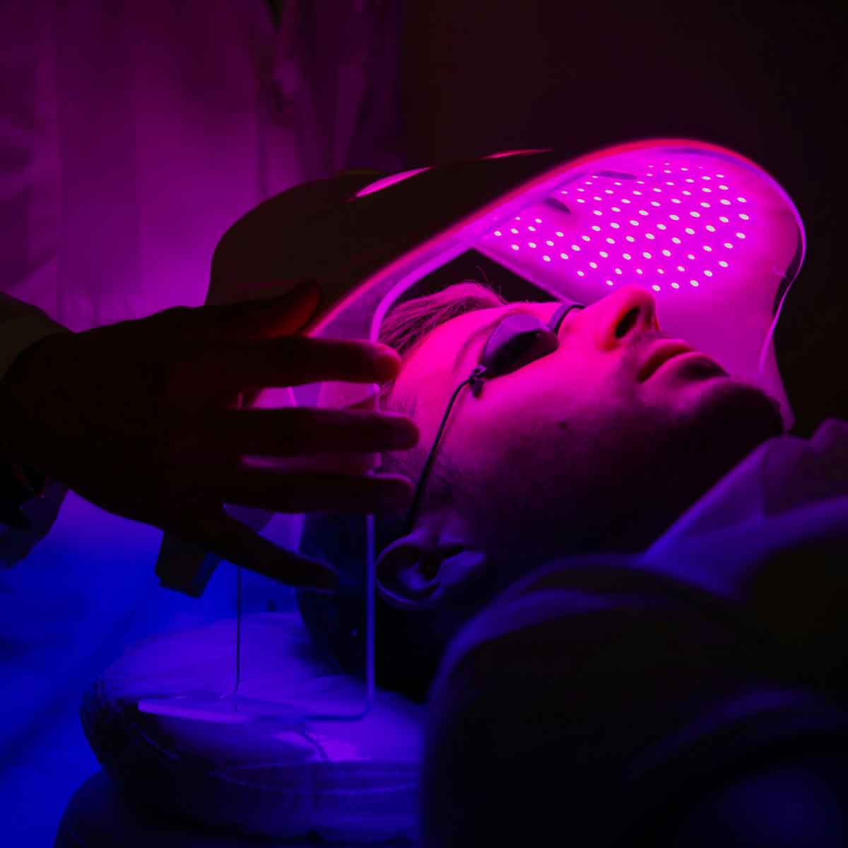 Close up of man bathed in purple light as he receives a laser facial treatment.