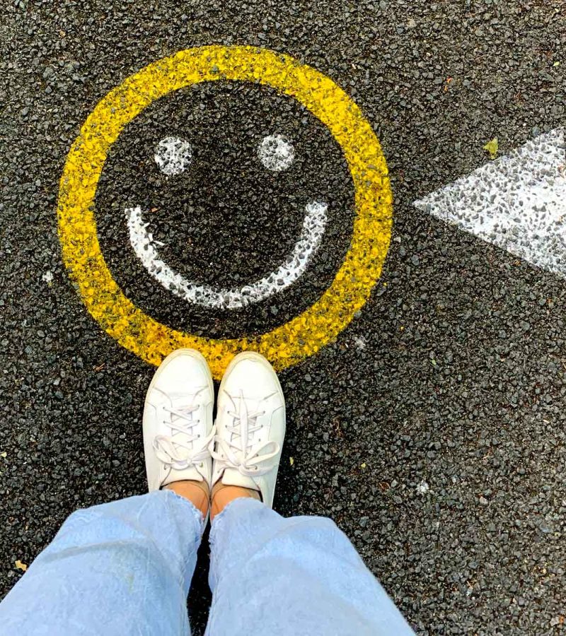 Top view of Happy face drawn out on pavement with feet standing on it.